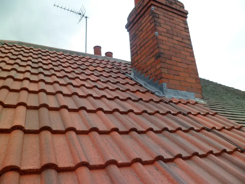 A repointed chimney with fresh lead flashing on a tiled roof by Tammat Group